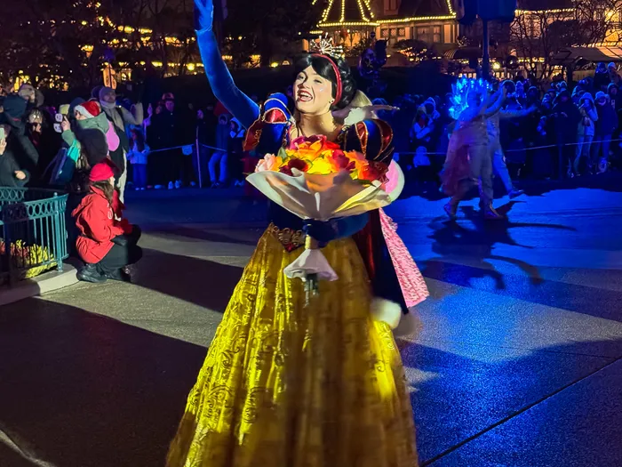 Blanche-Neige en robe dorée salue la foule le soir sur Main Street illuminée, pendant la parade de Noël