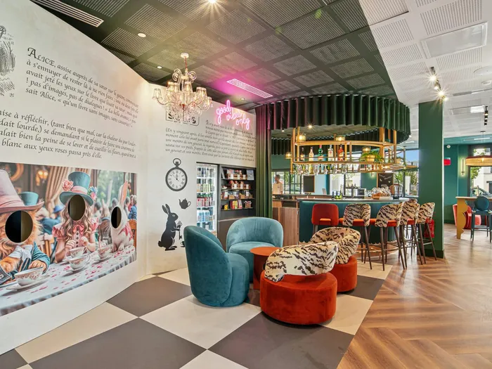 Salon lounge de l’Appart Hôtel All Suites Val d’Europe, fresque sur le thème d’Alice au pays des merveilles, fauteuils en velours et sol en damier.