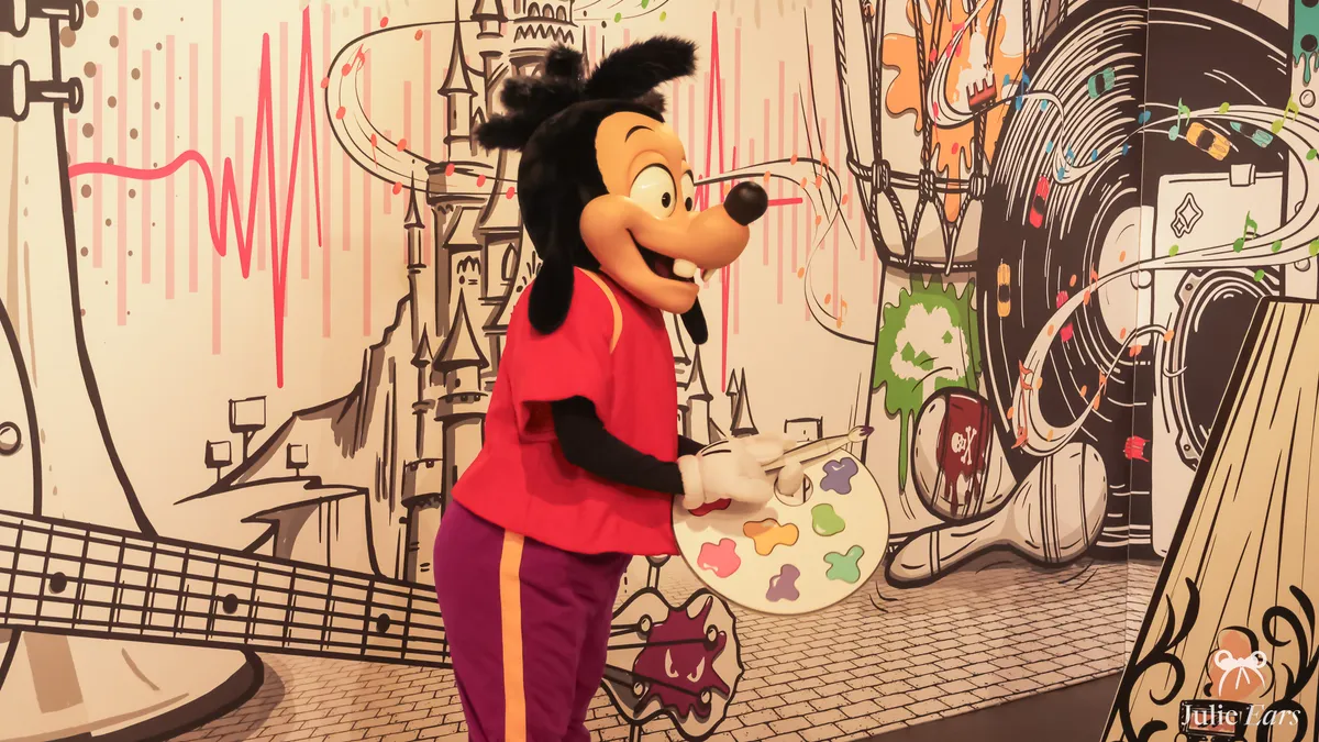 Max, Goofy’s son, with a painter’s palette and brush in front of a line-drawn mural, at a Pop-Up Surprises meet and greet for Disneyland Pass holders