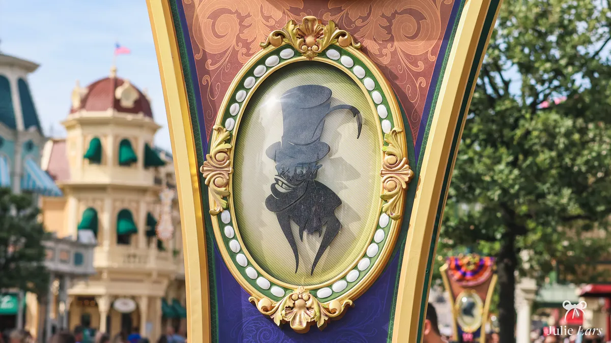 Gold medallion on a Halloween 2026 banner on Main Street U.S.A., showing the silhouette of a Villain in a top hat against colourful facades