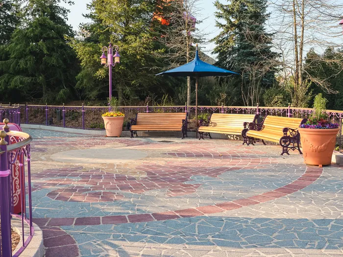 Esplanade aux pavés colorés bordée de bancs et de lampadaires violets, au petit matin sur Adventure Way.