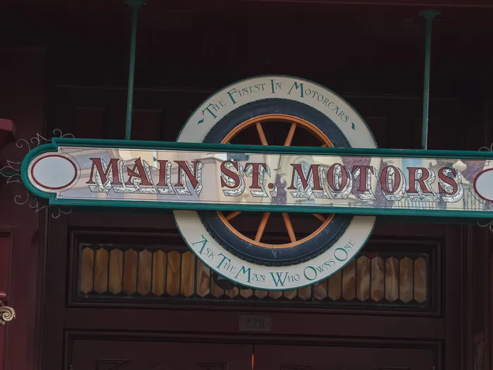 "Main St. Motors" sign reading "The Finest In Motorcars For The Man Who Owns One", with a spoked wheel, at Disneyland Paris.