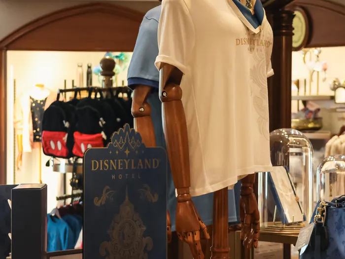 Polo blanc et foulard sur un mannequin en bois près d’un présentoir Disneyland Hotel.