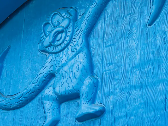 Stylised monkey carved in relief, with long hooked arms, on the blue-painted wooden plank wall of the Toy Story Playland shop at Disneyland Paris.
