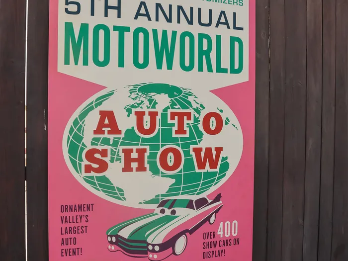 Affiche rose rétro « 5th Annual MotoWorld Auto Show » sur une palissade, sous le logo Cars de l’attraction.