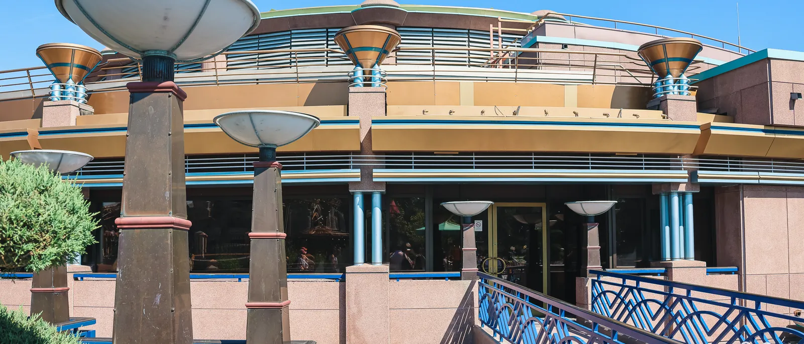 Bâtiment arrondi rétro-futuriste aux lampadaires en forme de disque et rampe à rambarde bleue, Disneyland Paris.