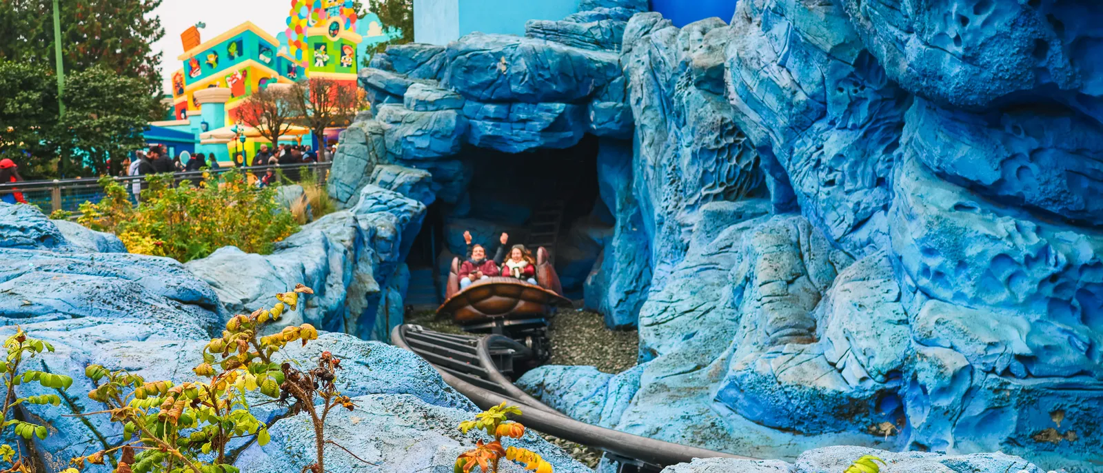 Wagon-tortue de Crush’s Coaster surgissant d’une grotte aux rochers bleus, passagers bras levés, Parc Disney Adventure World