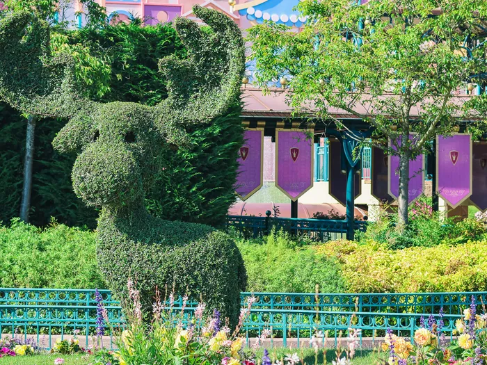 Buisson taillé en forme de faon devant la façade violette d’it’s a small world, jardins fleuris