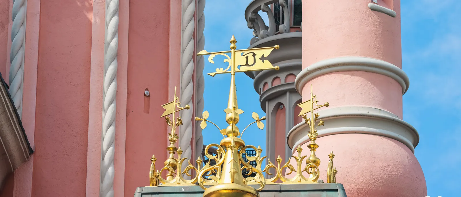 Girouette dorée marquée d’un « D » et toitures bleutées d’une tourelle rose du Château de la Belle au Bois Dormant, Disneyland Paris.