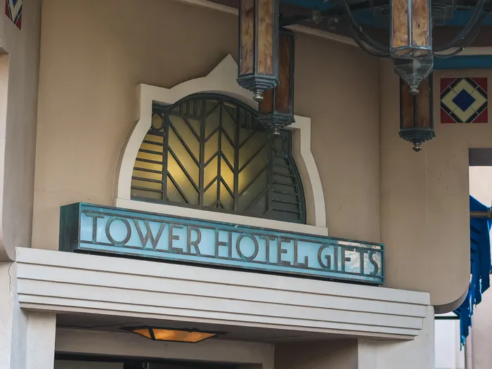 Art Deco "Tower Hotel Gifts" sign in patinated metal letters on a turquoise panel, above the shop entrance, at Disneyland Paris.