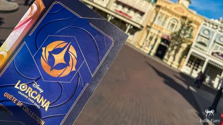 Blue and gold Disney Lorcana Collection Quest booklet held in a hand on Main Street U.S.A. at Disneyland Paris