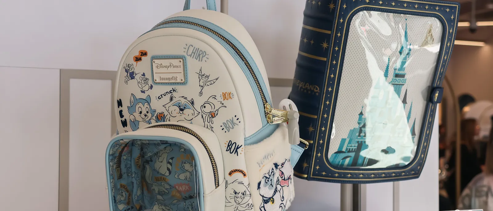 Deux sacs à dos Loungefly en boutique Disneyland Paris, un blanc à croquis Aristochats et un bleu au château.