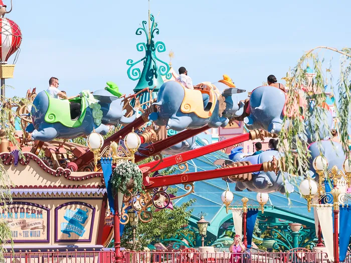 Visiteurs à bord des éléphants Dumbo en hauteur sous un ciel bleu, à Fantasyland au Parc Disneyland.