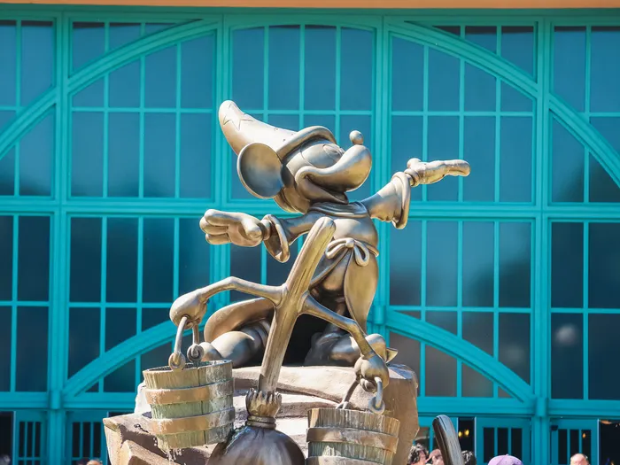 Statue en bronze de Mickey apprenti sorcier devant la façade vitrée turquoise de World Premiere Plaza.