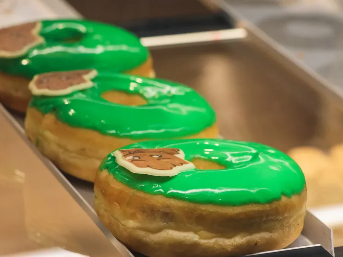 Trois donuts au glaçage vert décorés d’un ourson, alignés dans la vitrine du kiosque Searchlight