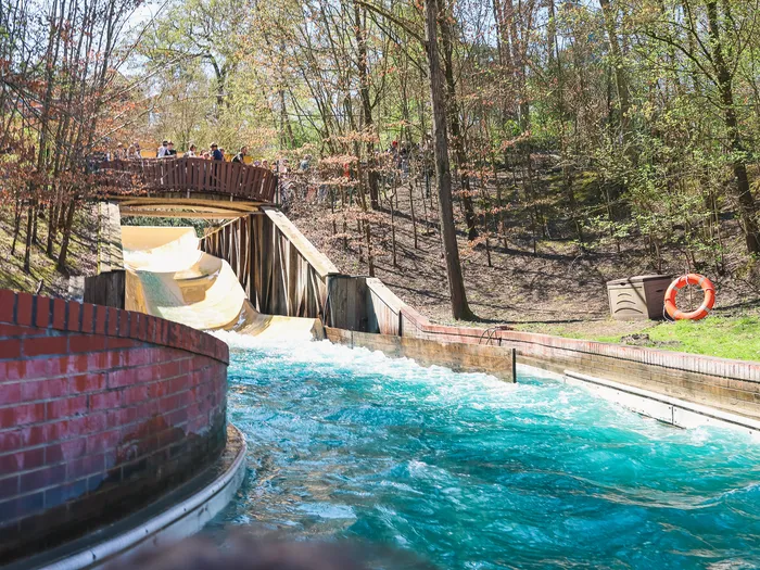 Bassin turquoise de l’Oxygénarium au pied de la descente en bois, mur de brique rouge et passerelle boisée en hauteur