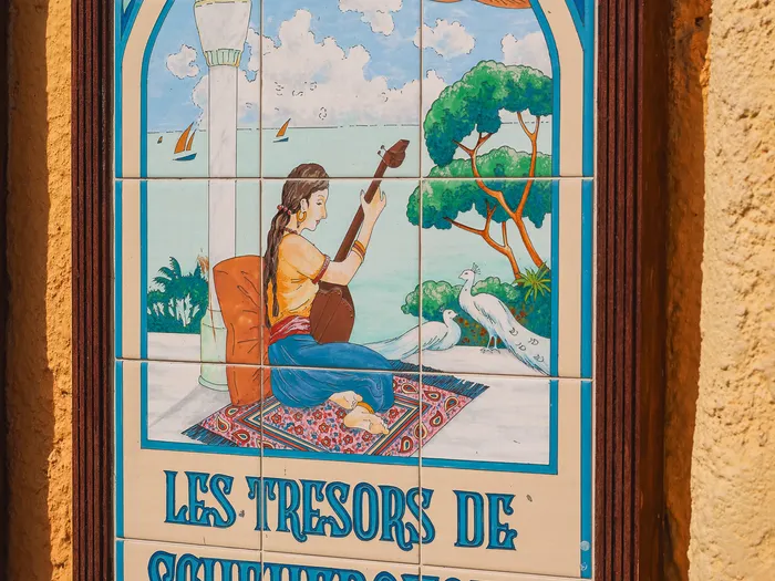Painted tile sign of Les Trésors de Schéhérazade at Disneyland Paris: a seated musician playing by the sea, surrounded by white peacocks