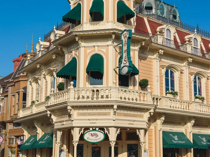Façade d’angle victorienne du restaurant Walt’s, tourelle à dôme rouge et stores verts, sur Main Street U.S.A.