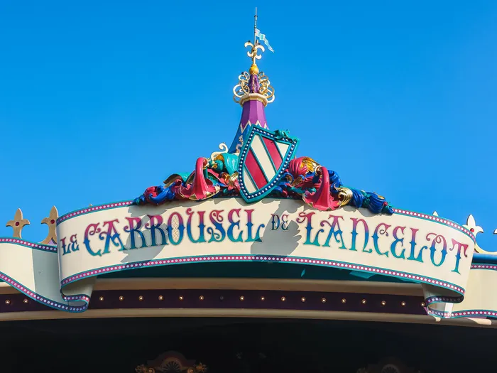 Fronton coloré portant l’enseigne « Le Carrousel de Lancelot », surmonté d’un blason, détaché sur un ciel bleu.