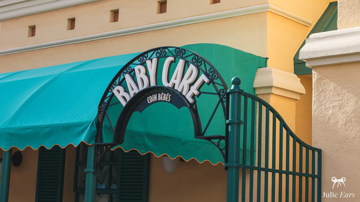 Wrought-iron "Baby Care" sign of the Baby Care Centre at Disney Adventure World, Disneyland Paris, in front of a green awning