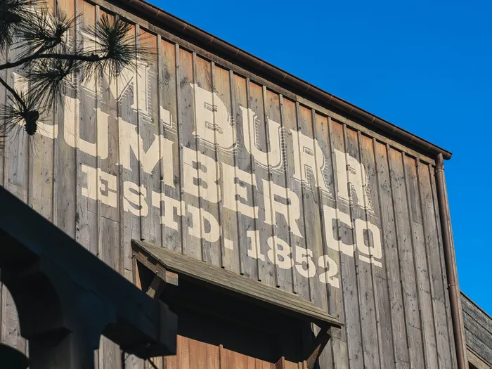 Large cream "Burr Lumber Co Estd. 1852" lettering on a wooden plank facade in Frontierland at Disneyland Paris, with a pine branch and a green lantern