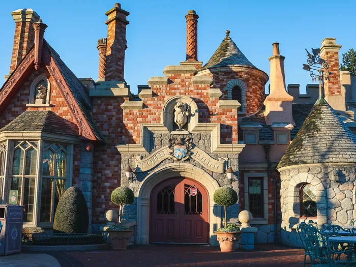 Manoir anglais en brique et pierre de Toad Hall, tourelles et cheminées, terrasse au soleil à Fantasyland.