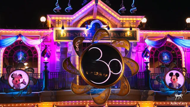 La gare de Disneyland Paris illuminée la nuit, ornée du logo doré des 30 ans du parc, avec Mickey et Minnie de part et d’autre.