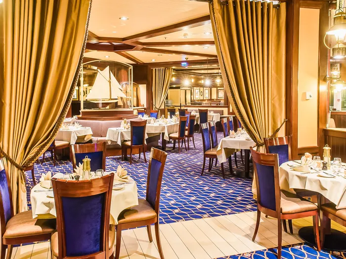 Salle nautique du restaurant Yacht Club : moquette bleue à motifs, voilier miniature et lanternes en laiton
