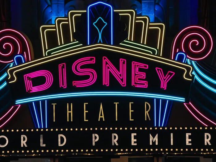 Enseigne néon rose et bleue du Disney Theater illuminée la nuit, à World Premiere Plaza.