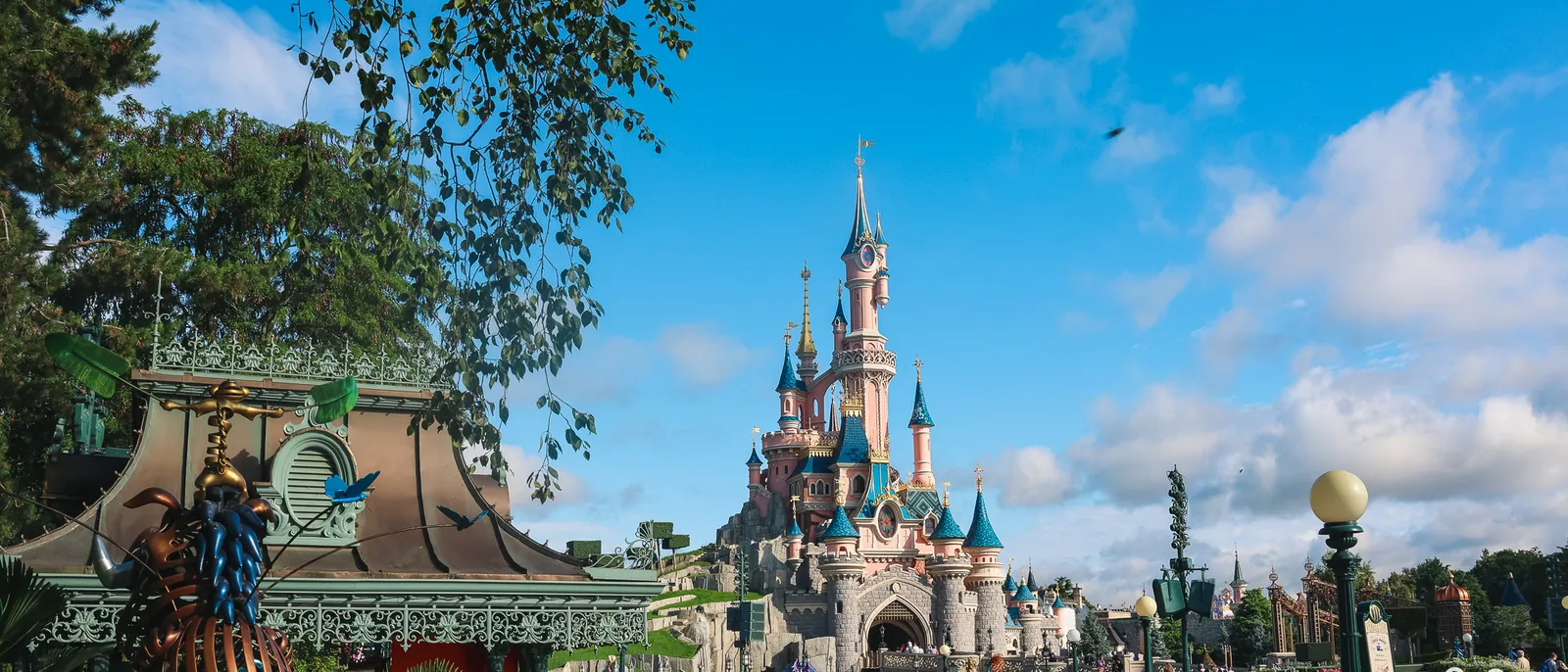 Le château rose de la Belle au Bois Dormant sous un ciel bleu nuageux, bordé d'arbres, à Disneyland Paris.