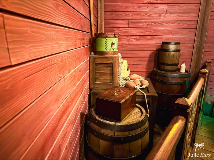 Décor de la file d'attente de Frozen Ever After avec tonneaux en bois, coffres et boîte peinte contre un mur de planches rouges.