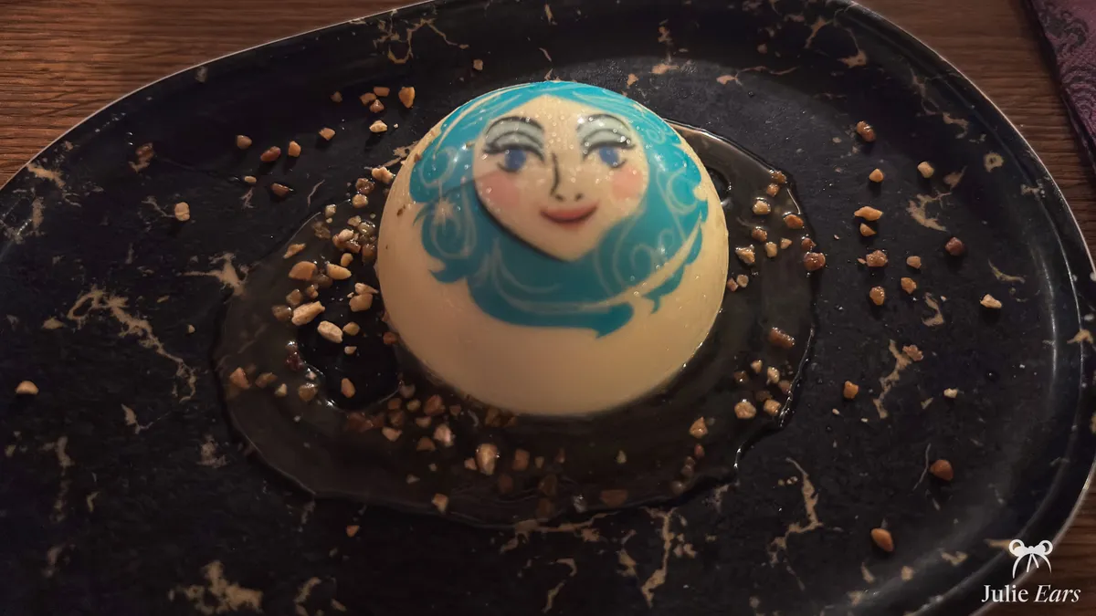 White dome dessert with a pale, blue-haired face on a black marbled plate with gold flakes, Unlucky Nugget Saloon, Frontierland, Halloween 2025