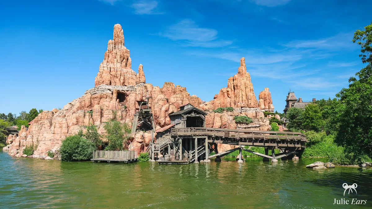 Big Thunder Mountain at Disneyland Paris across the Rivers of the Far West: red rock peaks, wooden mine buildings on stilts and Phantom Manor beyond
