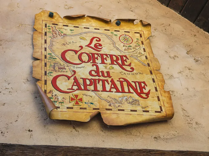 Treasure map-shaped sign bearing the name Le Coffre du Capitaine, fixed to a rendered wall at Disneyland Paris