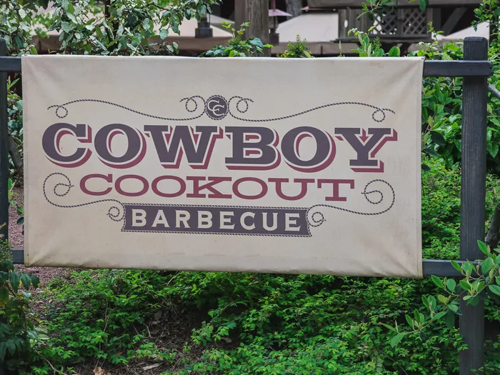 Enseigne en toile Cowboy Cookout Barbecue accrochée dans la verdure, à Frontierland