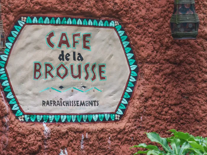 Enseigne murale en mosaïque du Café de la Brousse à Adventureland, sur un mur d’argile ocre.