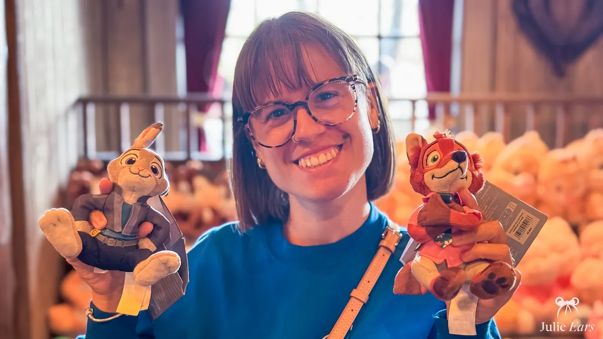 Julie Ears holding two shoulder plushes from Zootropolis, Judy Hopps and Nick Wilde, in a shop at Disneyland Paris.