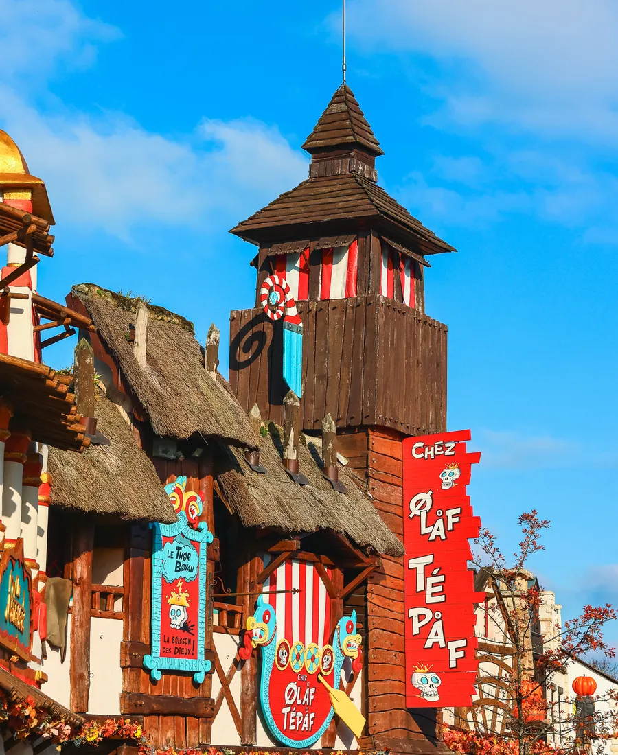 Façade à colombages et toit de chaume de Chez Ólàf Tépàf, enseigne verticale rouge et tour de bois viking