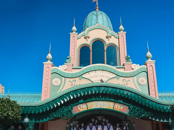 Turquoise dome and small bell tower of Café Luminosity at Disneyland Paris seen from below against a blue sky