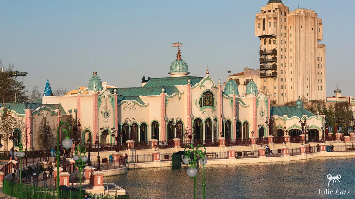The Regal View Restaurant at Disneyland Paris, cream and pink with pale green domes on the lakeside, the Tower of Terror behind, in golden light