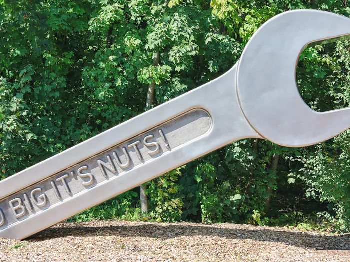Immense clé à molette métallique gravée « So Big It’s Nuts! » posée dans la végétation, décor de Cars ROAD TRIP.