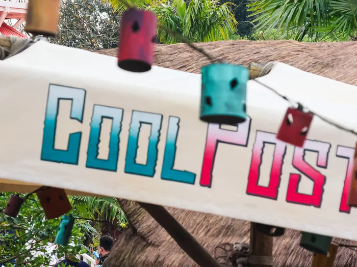 Enseigne peinte Cool Post sur une bâche claire, pots suspendus et toit de chaume à Adventureland