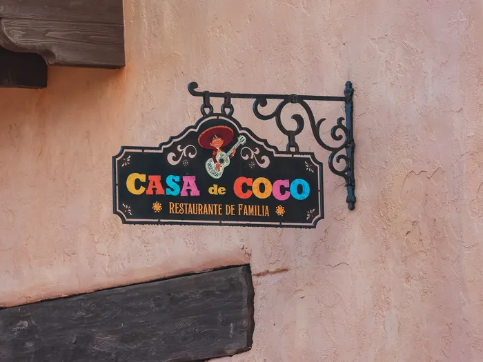 Petite enseigne suspendue en fer forgé du Casa de Coco, Miguel à la guitare, sur une façade rose de Frontierland