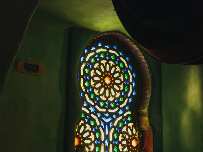 Vitrail en rosace aux motifs bleus et verts éclairé dans un mur vert du Passage Enchanté d’Aladdin