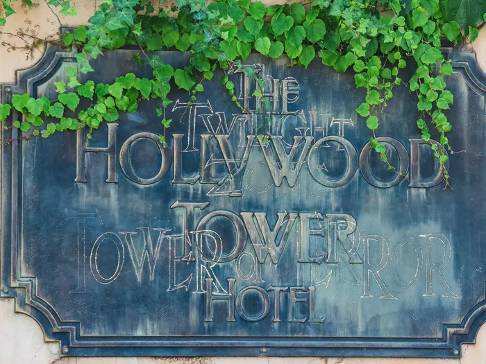 Plaque de bronze patinée « The Twilight Zone Hollywood Tower Hotel » couverte de lierre sur un mur fissuré du Tower of Terror.