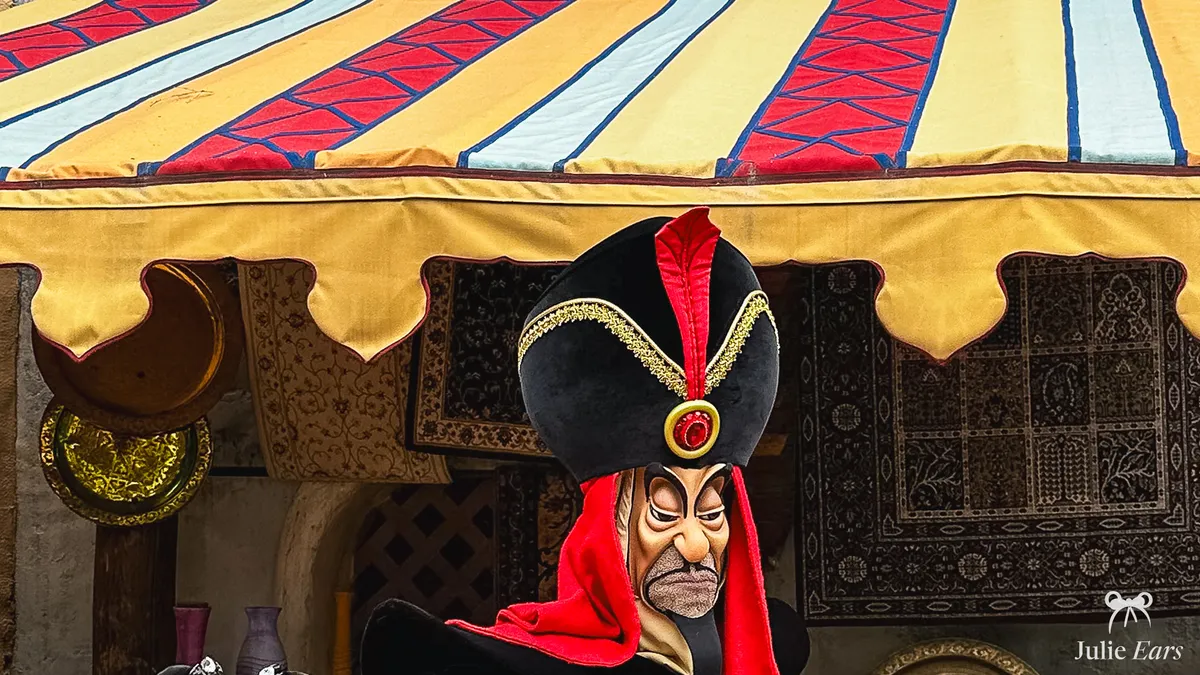 Jafar, in a black hat with a red feather and a menacing look, under a tent of the Agrabah bazaar at Disneyland Paris.