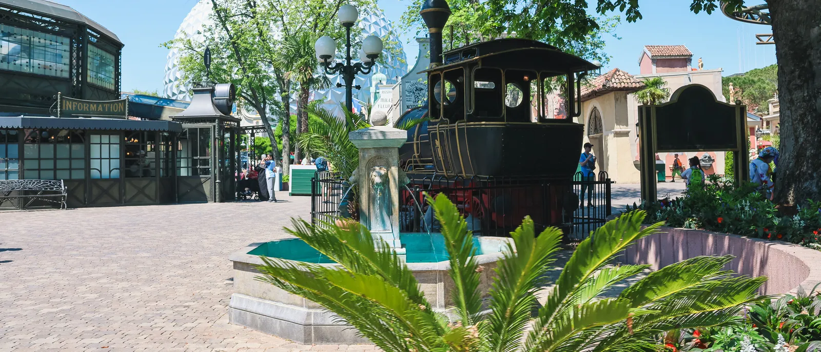 Ancienne locomotive noire exposée sur une place pavée avec lampadaires et palmiers à Europa-Park