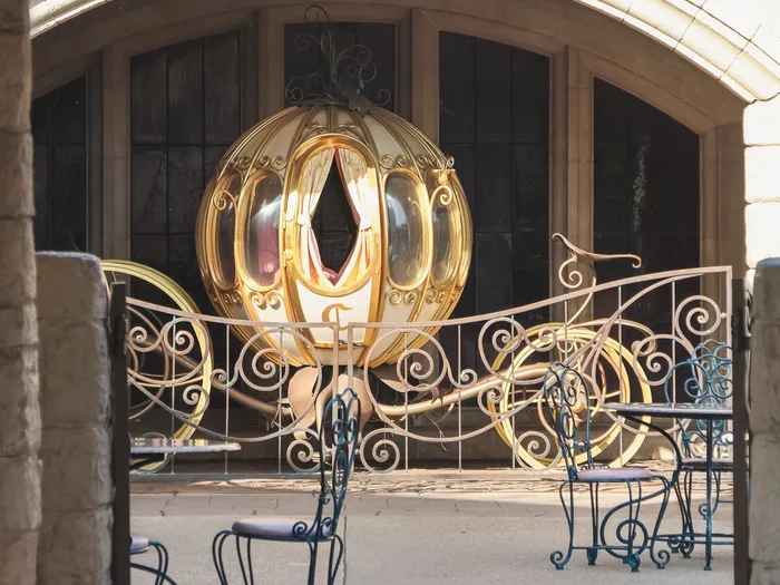 Carrosse citrouille doré derrière une grille en fer forgé, vu sous l’arcade de l’Auberge de Cendrillon