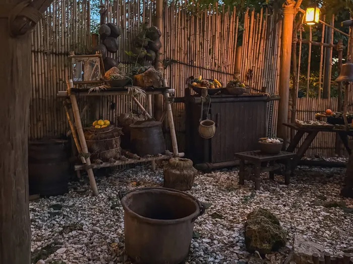 Coin campement avec clôture de bambou, marmite et paniers de fruits éclairés au crépuscule, La Cabane des Robinson