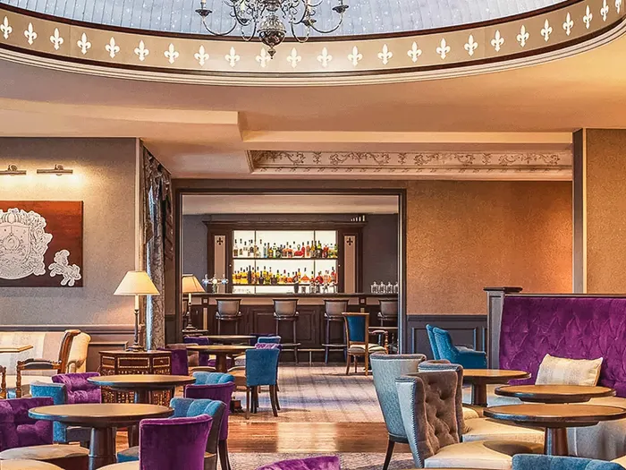 Salon feutré du Fleur de Lys Bar du Disneyland Hotel, fauteuils violets et bleus, lustre et comptoir au fond.
